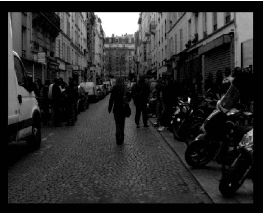 Black-and-white still from the film of two people walking through the streets of Paris